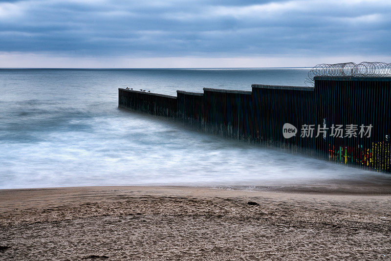 海滩和海浪的近景日落附近的国际边界墙在Playas Tijuana，墨西哥